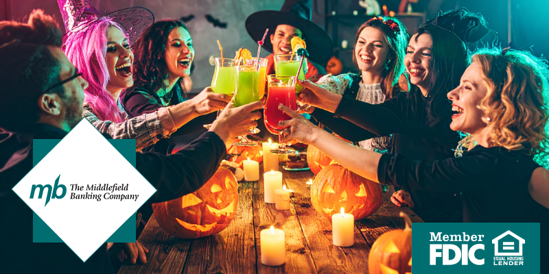 Adults at a table lifting alcoholic beverages in cheers while wearing Halloween costumes